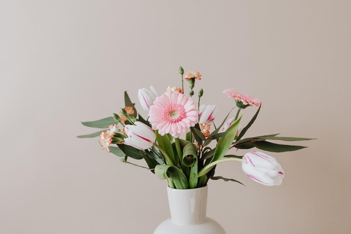 Light bouquet of fresh tulips with green leaves arranged with pink Gerberas and yellow red carnations in white ceramic vase